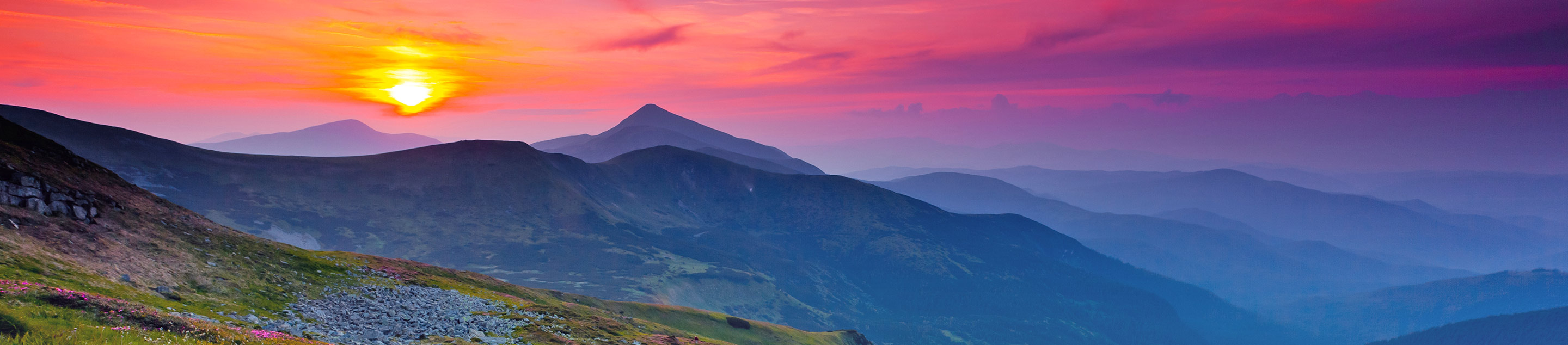 Sunset over an alpine meadow with silhouetted mountains in the background.
